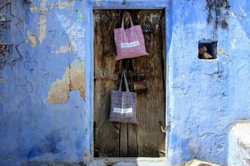 Image of Raspberry and Midnight BLue Monnsoon Bedding bags hanging on a rustic door surrounded by Jodhpur Blue walls